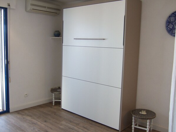 A room with a white wardrobe, a small round table, and a blue decorative plate on the wall. - Large studio with terrace, sea view, all comforts, near Collioure, private parking (Port-Vendres)