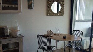 Un comedor con una mesa de madera, dos sillas negras de malla metálica, un armario blanco con microondas y un espejo decorativo en la pared.
