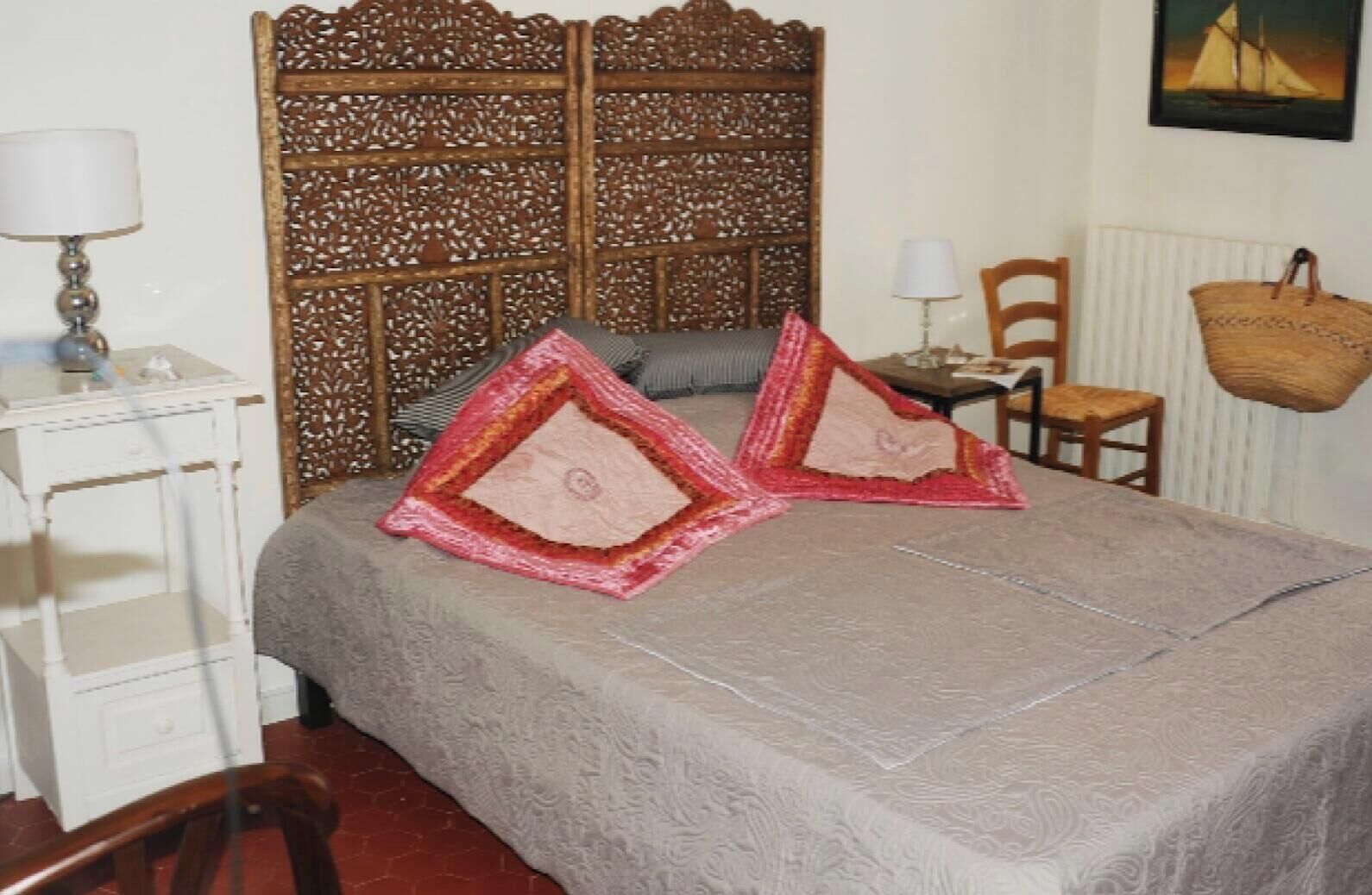 Une chambre à coucher comprenant un lit, deux oreillers, une table de chevet, une lampe, une chaise, une fenêtre et un panier fixé au mur.