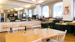 Un café moderno con mesas de madera y sillas blancas, una barra de café y diversos mostradores con comida.