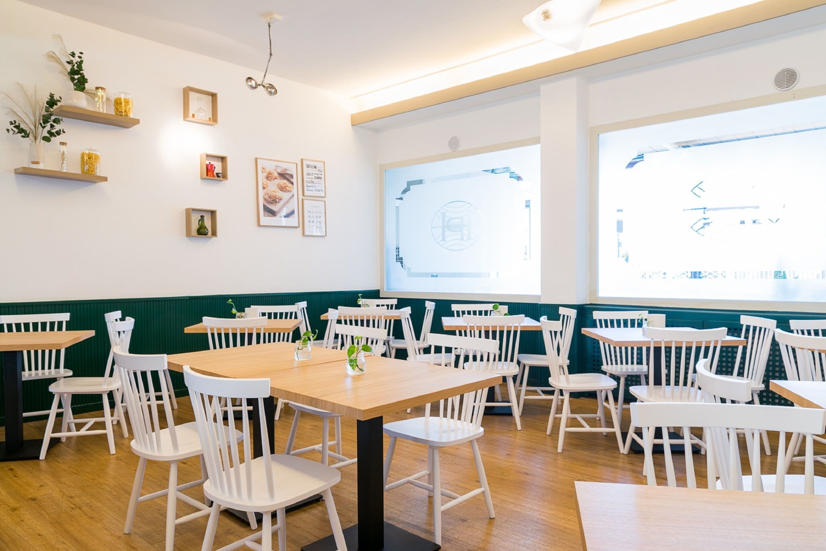 A dining area with white chairs and tables, wooden shelves with decorative items, and a large window with a view.