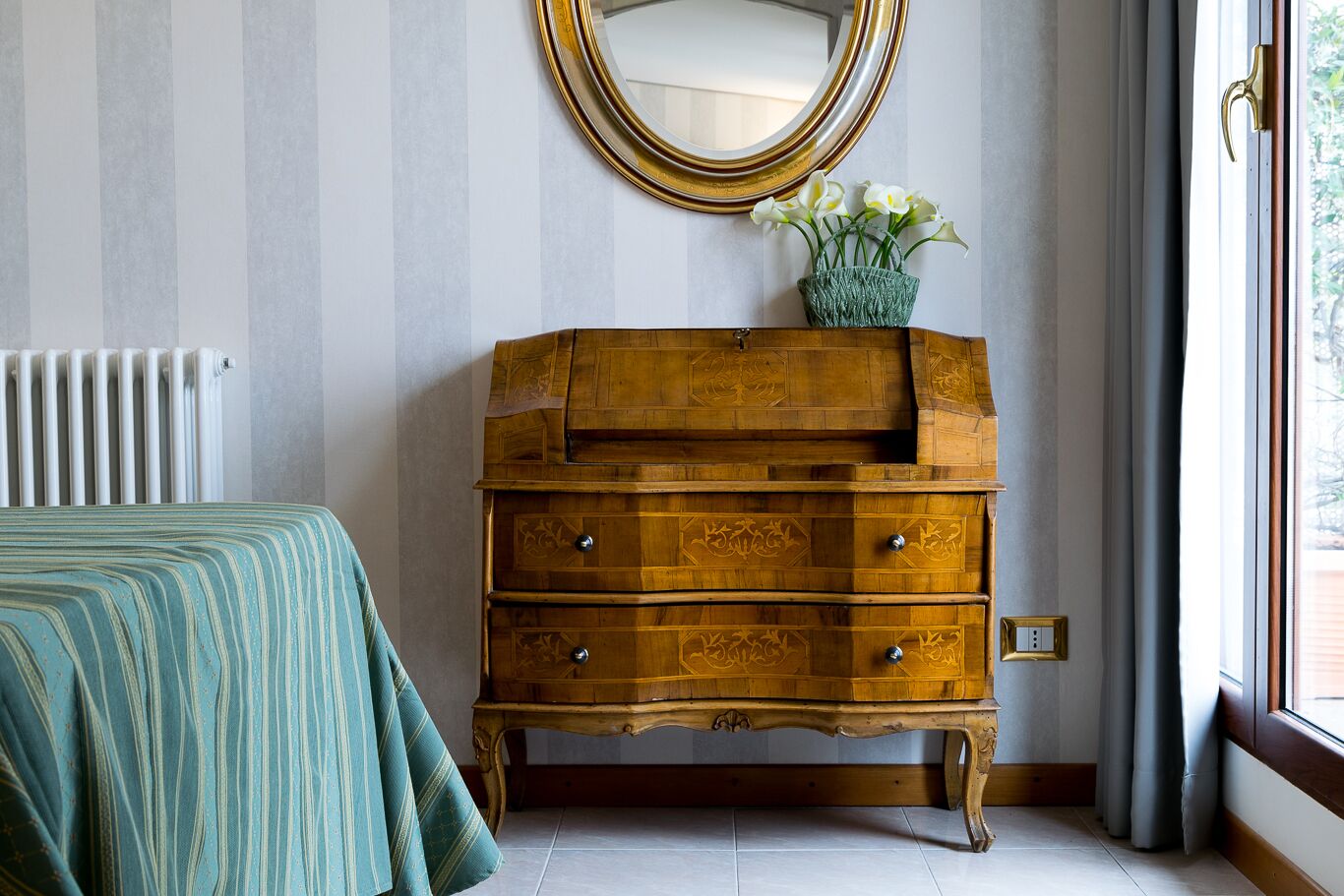 A room with a bed, a wooden dresser with drawers, a mirror, and a radiator.