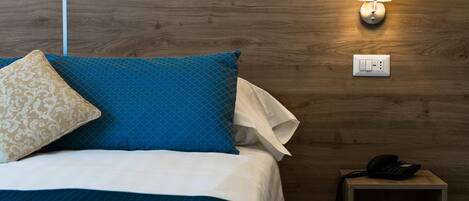 A neatly made bed with blue and beige pillows, a bedside lamp, and a phone on a wooden nightstand.