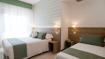 A hotel room with two beds, a wooden headboard, a patterned wall, and a window with sheer curtains.