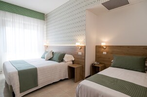 A hotel room with two beds, a wooden headboard, a patterned wall, and a window with sheer curtains.