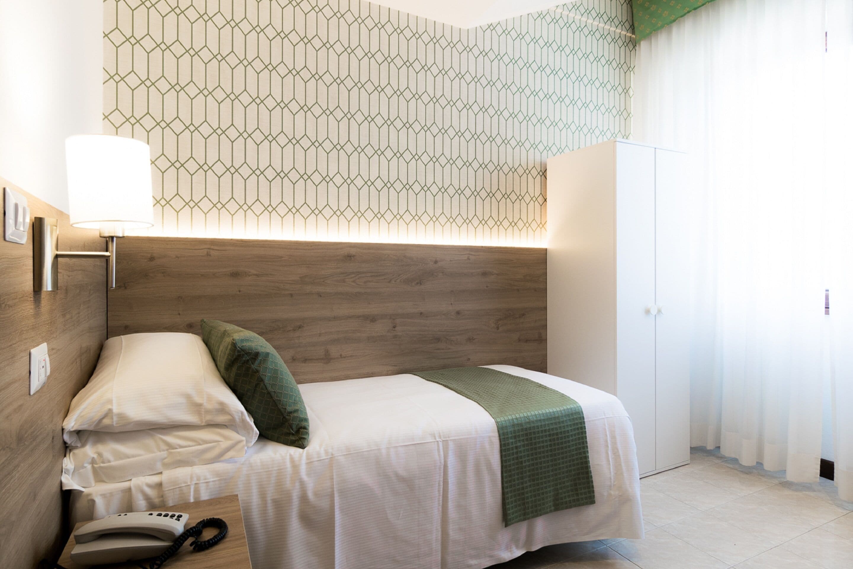 A neatly arranged bedroom with a wooden headboard, a bedside lamp, a telephone, and a green throw blanket.