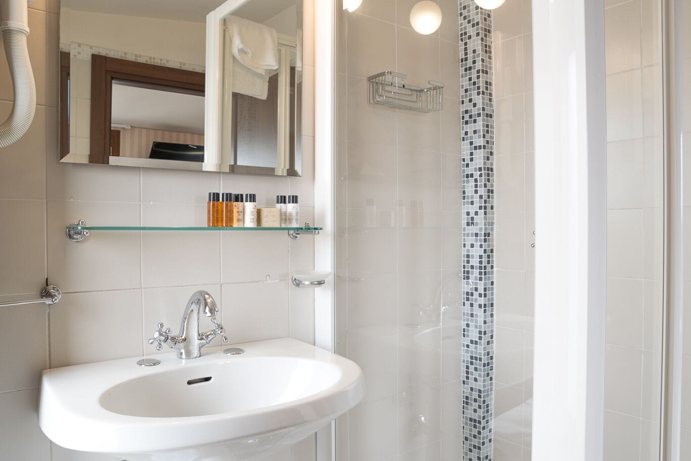 A modern bathroom with a white sink, a mirror, and a shower with a mosaic tile design.