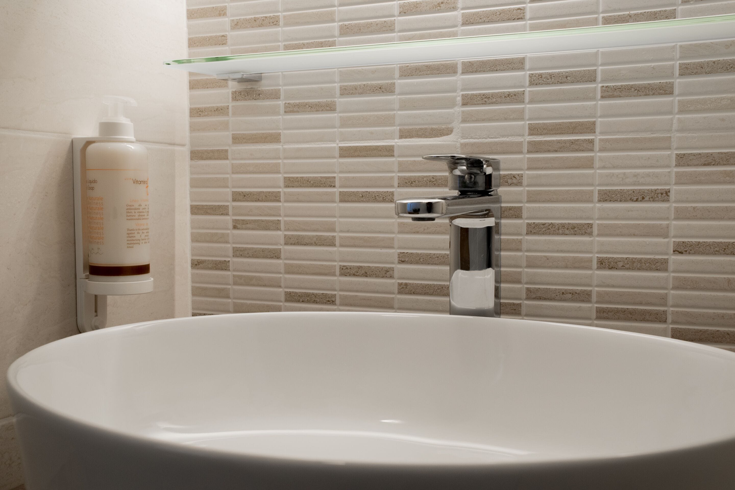 A bathroom with a freestanding bathtub, a glass shelf above the tub, and a bottle of shampoo on the wall.