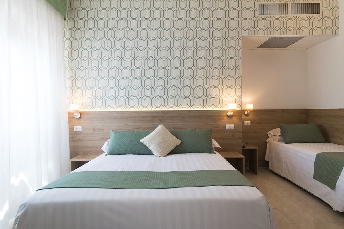 Hotellihuone, jossa on kaksi sänkyä, kuviollinen seinä ja puinen pääty.
