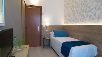 A hotel room with a bed, a bedside table, a TV, and a wall with geometric patterns.