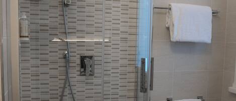 A modern bathroom with a glass-enclosed shower, a white pedestal bidet, and tiled walls.