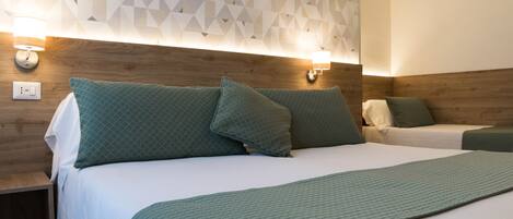 Habitación de hotel con cabecera de madera, dos camas con ropa de cama verde y decoración de pared con motivos geométricos.