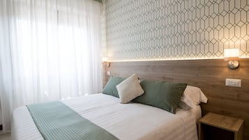 A neatly made bed with a green throw, a wooden headboard, and a geometric-patterned wall.