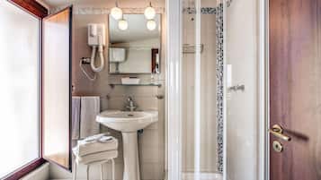 Une salle de bain avec une douche à parois de verre, un lavabo sur colonne, un miroir avec éclairage intégré et un porte-serviettes.