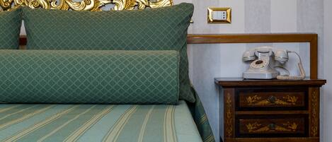 A bed with green patterned bedding, a wooden nightstand with a rotary phone, and a gold ornate headboard.
