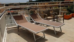 Terraza en la azotea con dos tumbonas y una silla, con vistas a un paisaje urbano que incluye edificios y una estructura en forma de cúpula.