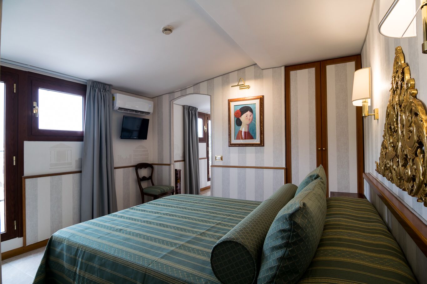A hotel room with a bed, a chair, a television, a painting, and a decorative wall piece.