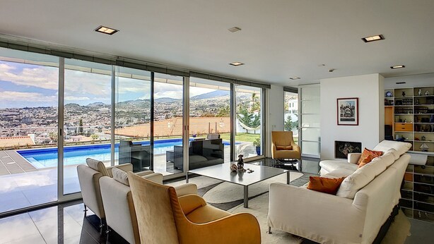 Ein modernes Wohnzimmer mit Glaswand, Pool und Blick auf die Stadt.