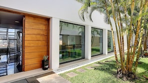 Ein modernes Haus mit großen Glasfenstern, einer Holztür und einem kleinen Garten mit Palmen.