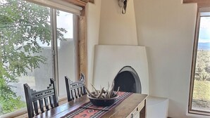 A rustic interior with a wooden dining table, chairs, a fireplace, and a large window.