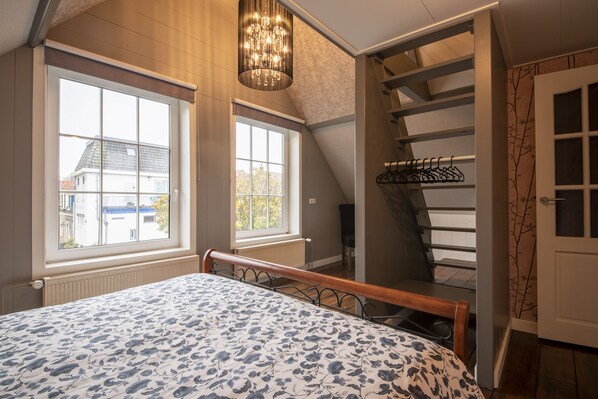 Una camera da letto con un letto, due finestre, un termosifone, un lampadario e una scala.