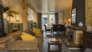 A cozy living room with a fireplace, a dining area, and a kitchen with green cabinets and a tiled backsplash.
