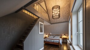 A bedroom with a wooden staircase, a bed with patterned bedding, bedside lamps, and a chandelier.