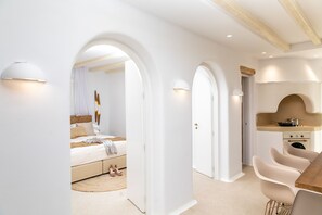 Een moderne, minimalistisch ingerichte slaapkamer met een groot bed, een kleine keukenhoek en een eethoek met stoelen.