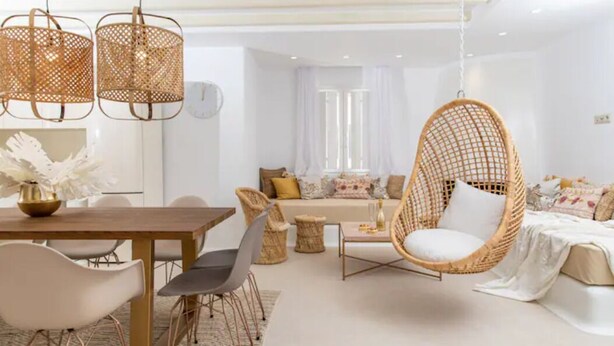 Ein modernes Wohnzimmer mit Essbereich, ausgestattet mit Rattanmöbeln, einem Hängestuhl und einer Couch mit Kissen.