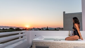 Eine Frau sitzt in einer Badewanne auf einem Balkon mit Blick auf einen Sonnenuntergang.