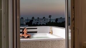 Eine Frau entspannt in einer Badewanne auf einem Balkon mit Blick auf die Stadt bei Dämmerung.