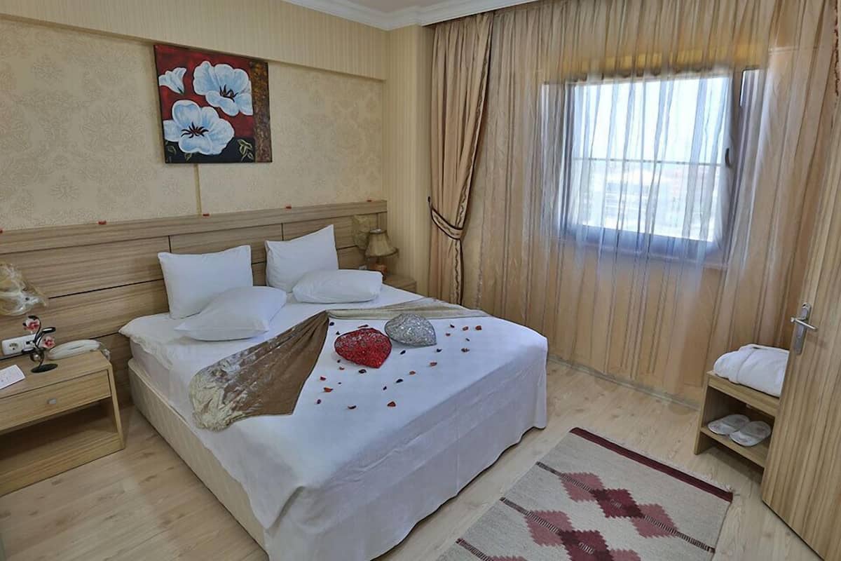 Une chambre d’hôtel avec un grand lit, une table de chevet, une lampe, un tableau et une fenêtre avec des rideaux.