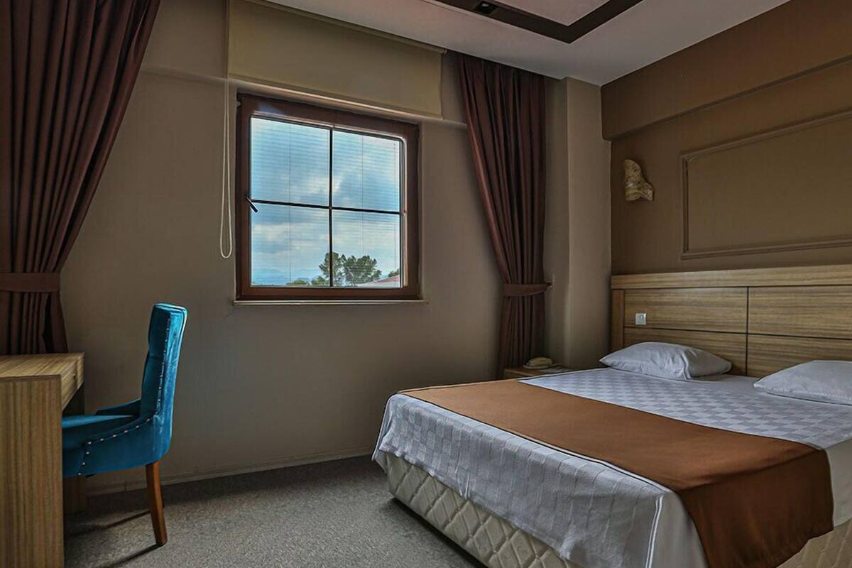 Une chambre d’hôtel avec un lit, un bureau, une chaise et une fenêtre avec des rideaux.