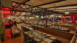 Un restaurant spacieux doté de plusieurs espaces de restauration, notamment une longue table conviviale et plusieurs petites tables.