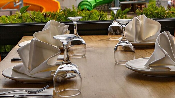 Une table à manger dressée avec des assiettes et des verres à vin, donnant sur un parc aquatique avec des toboggans colorés.