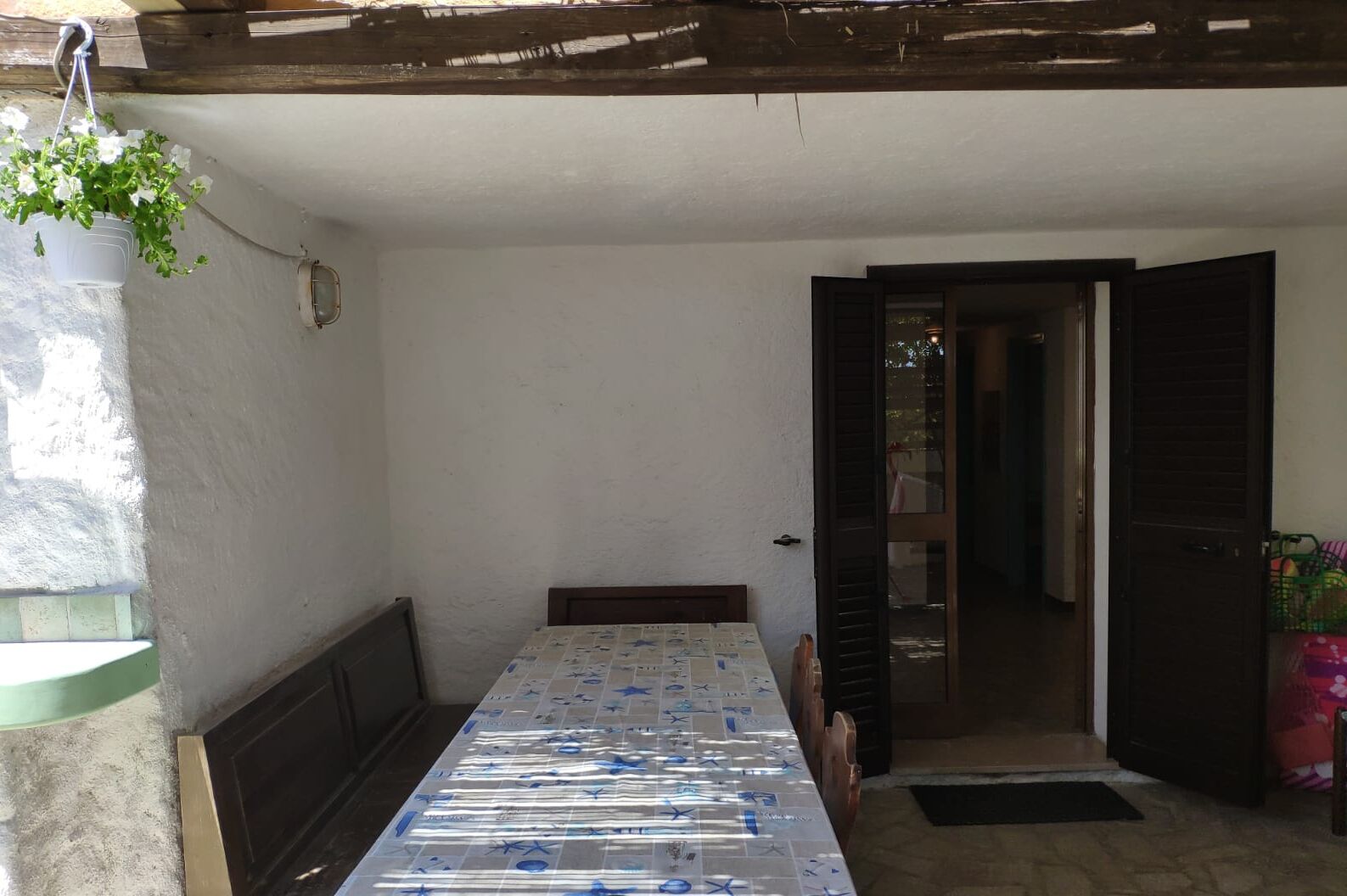 Ein kleiner, abgeschlossener Patio-Bereich mit Tisch und Stühlen, einer hängenden Pflanze und einer Tür zu einem Außenbereich.