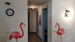 A hallway with white walls, a clock, and two paintings of flamingos.