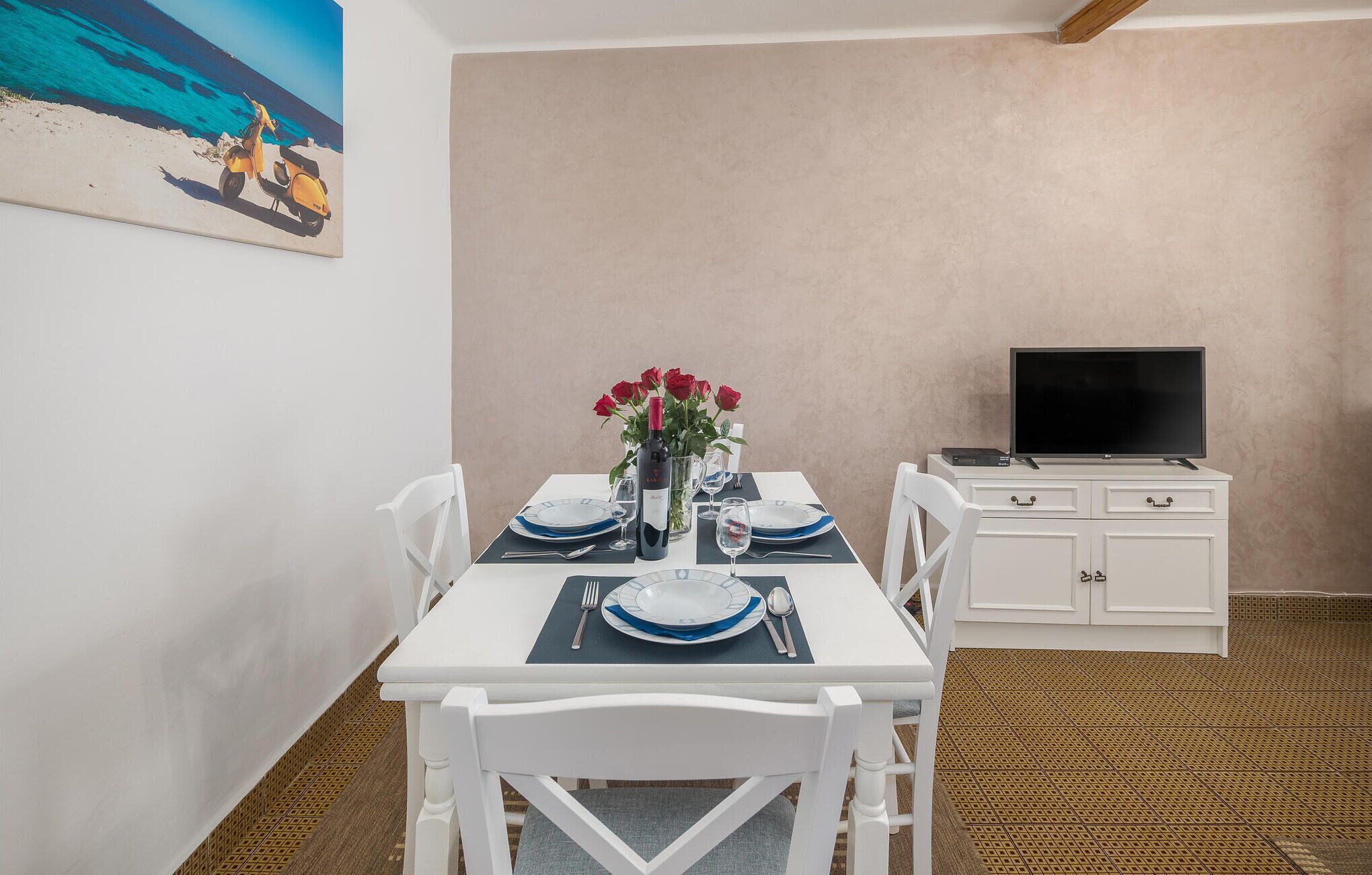A dining area with a table set for four, a television, and a painting of a beach scene.