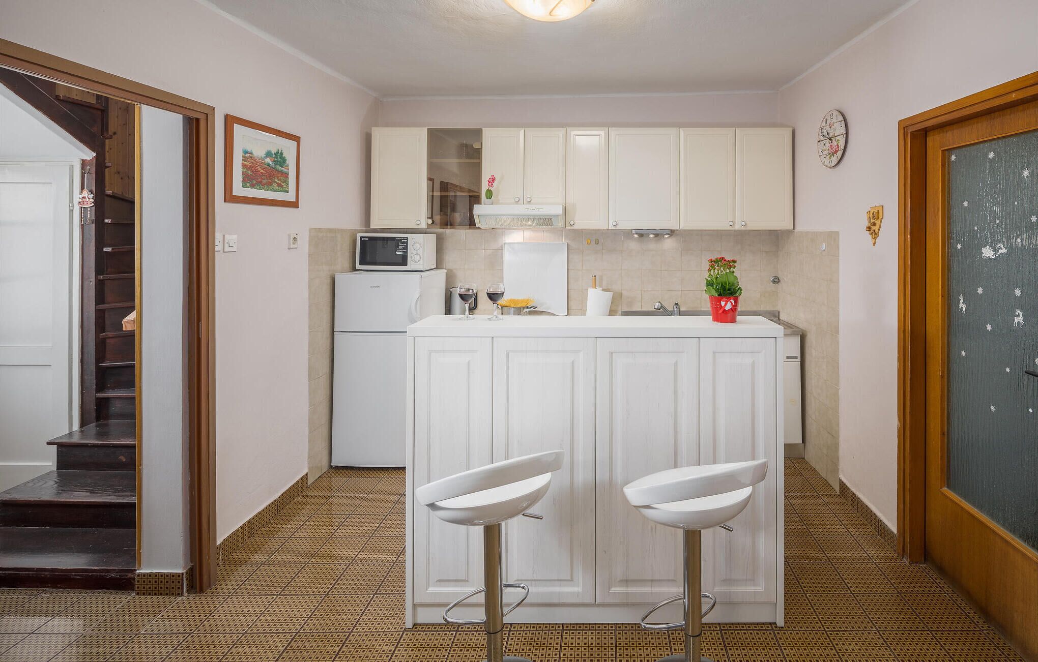Uma cozinha compacta com armários brancos, micro-ondas, pia e dois banquetas.