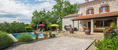Una casa de piedra con piscina, mobiliario exterior y zona de barbacoa.