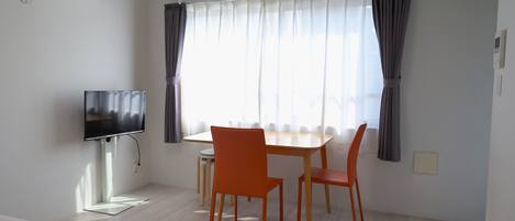 A hotel room with a bed, a TV, a dining table with chairs, and a window with curtains.