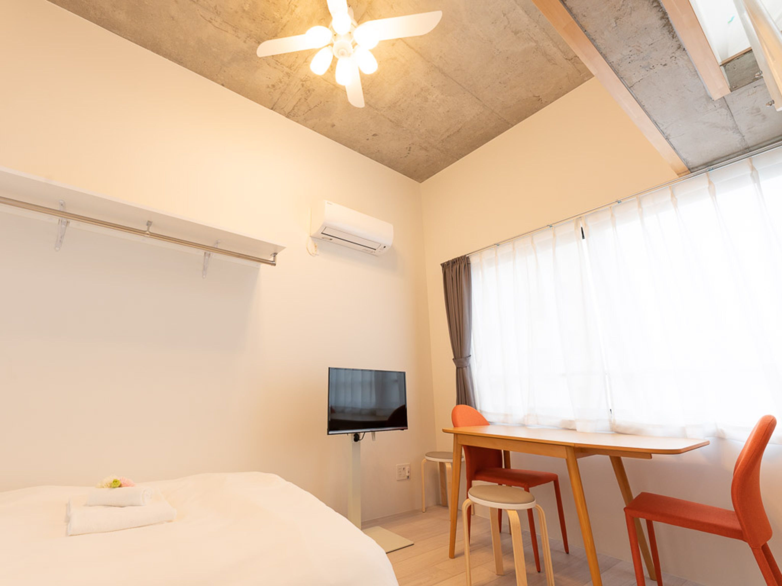 Una habitación de hotel moderna con cama, escritorio, dos sillas, televisión y ventilador de techo.