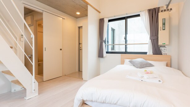 A hotel room with a wooden bed, a window with curtains, a staircase, and a wall-mounted air conditioning unit. - Laffitte Ryogoku (Tokyo)