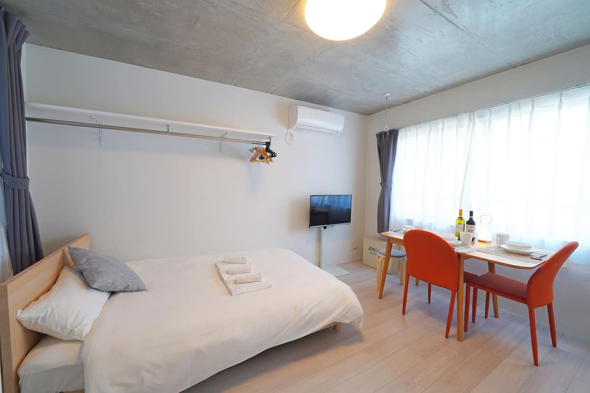 Quarto de hotel com cama, televisão, mesa de jantar com cadeiras e janela com cortinas.