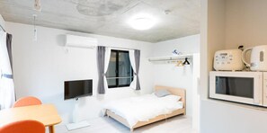 Une petite chambre moderne équipée d’un lit, d’une télévision, d’un four à micro-ondes et d’une table avec des chaises.