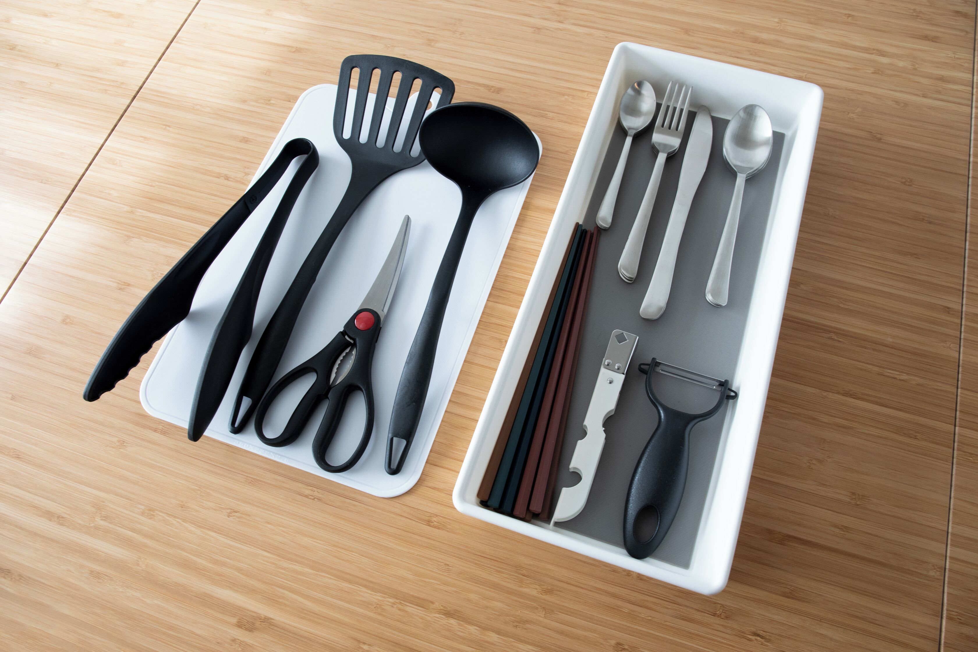 A kitchen drawer with various utensils including a spatula, spoon, knife, and scissors.