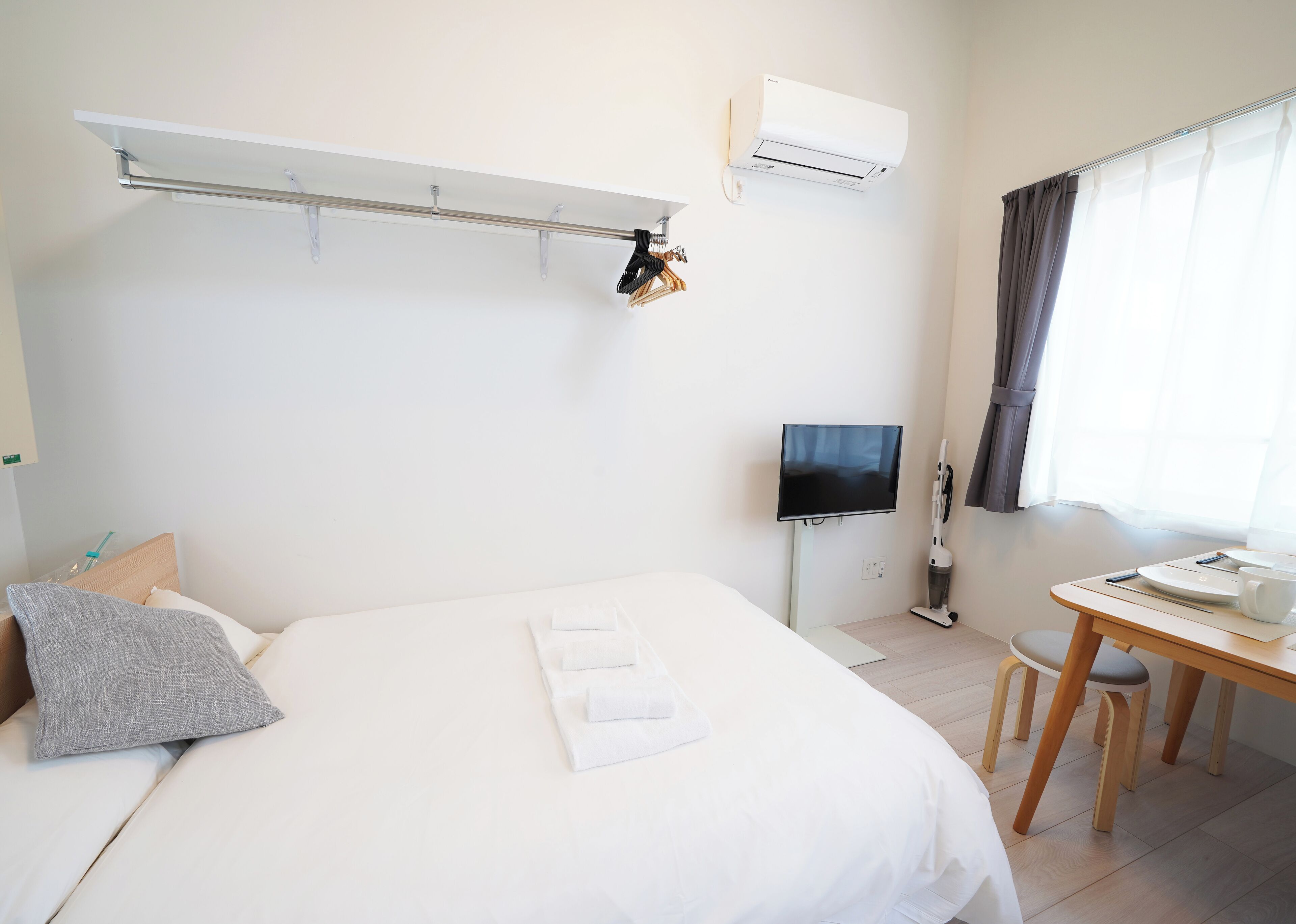 A hotel room with a bed, a desk with a chair, a TV, and an air conditioning unit.
