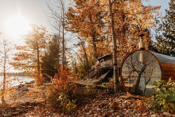 Eine rustikale Holzhütte mit einer Holzterrasse, umgeben von Herbstlaub und Blick auf einen See.