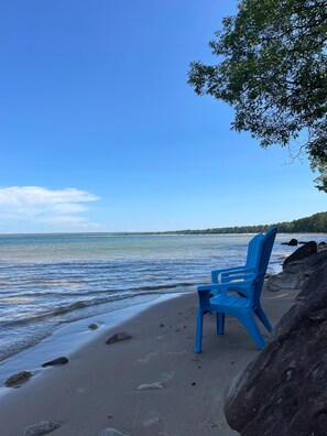 Ein Strand mit einem blauen Plastikstuhl und einem großen Felsen.