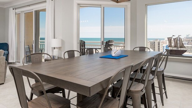 A dining area with a large table and chairs, a hanging light fixture, and large windows with a view of the ocean. - Beautiful 3 bedroom, 3 bath condo is located in the popular luxury building, Gateway Grand (Ocean City)